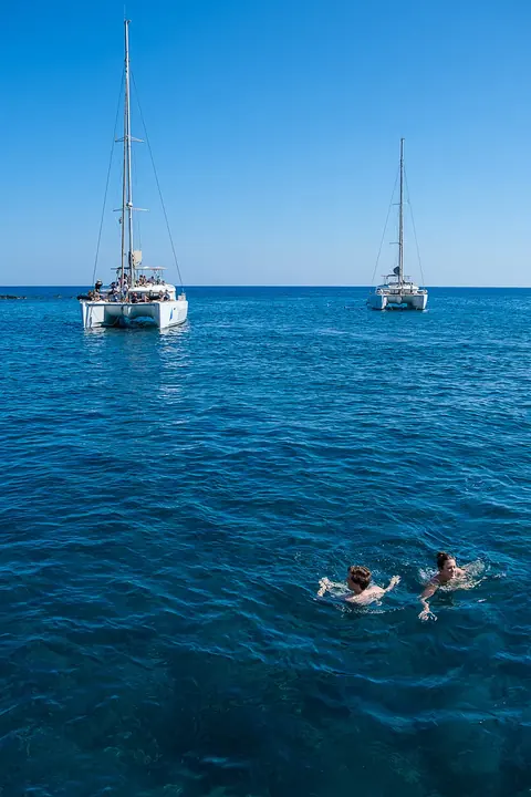 Two catamarans anchored in deep blue water with two swimmers between them, seen from above