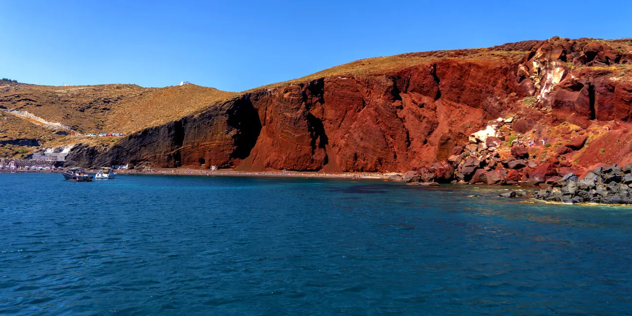 Red Beach from the water — crimson lava cliffs over dark sand