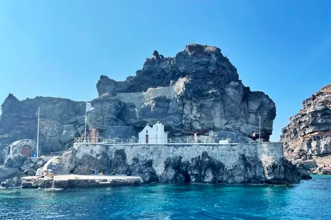 The white chapel of St. Nicholas on its rocky islet off Oia, with a Greek flag and a small landing stage