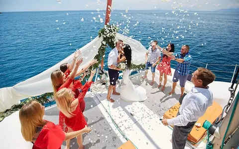 A wedding party throwing petals over the couple on the bow net of the catamaran