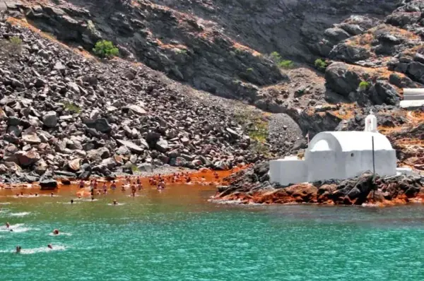 Swimmers in the warm, rust-colored water of the Hot Springs beside the white chapel on Palea Kameni