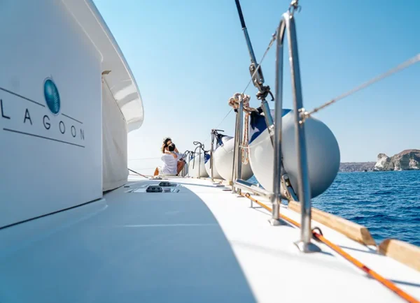 The side deck of the Lagoon catamaran with its fenders, a guest sitting at the bow and the pale cliffs ahead