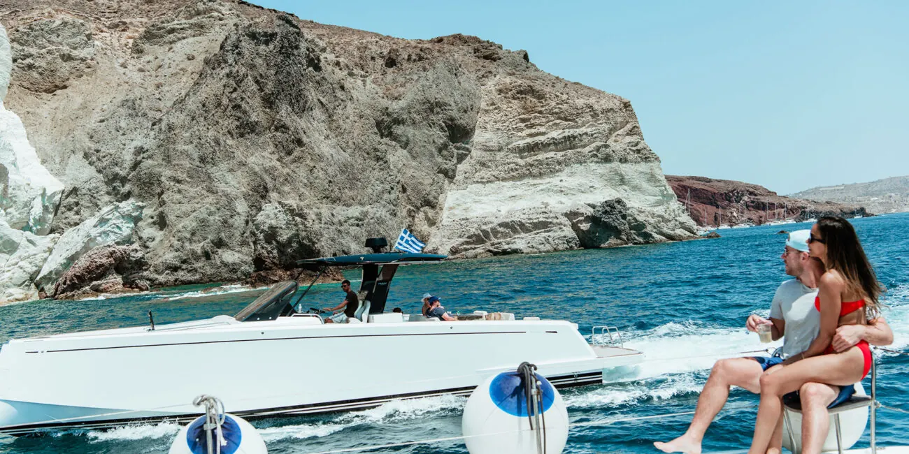 A speedboat running alongside our catamaran below Santorini's cliffs — private boat tours and water-taxi runs