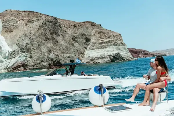 A speedboat running alongside our catamaran below Santorini's cliffs — private boat tours and water-taxi runs
