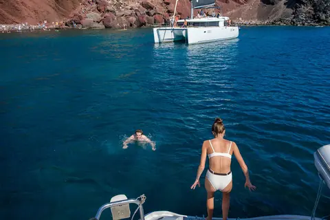 The Lagoon catamaran anchored off Red Beach, one guest swimming and another on the stern steps