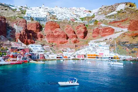Ammoudi Bay below Oia: red cliffs, fish tavernas at the water's edge, the white houses of Oia on the rim and a small boat heading in