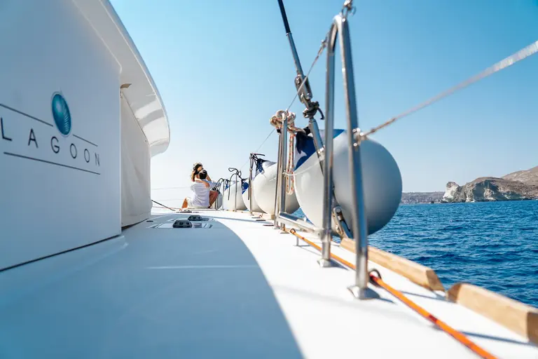 The side deck of the Lagoon catamaran with guests at the bow and the south-coast cliffs ahead