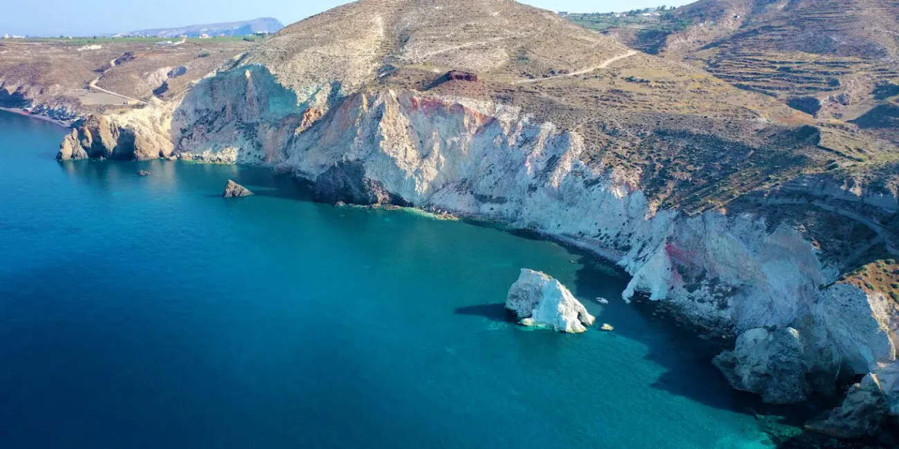 Santorini's white volcanic coast from the water — where our island crossings begin